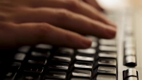 Close-up of fingers typing quickly on a backlit keyboard, focus on hands