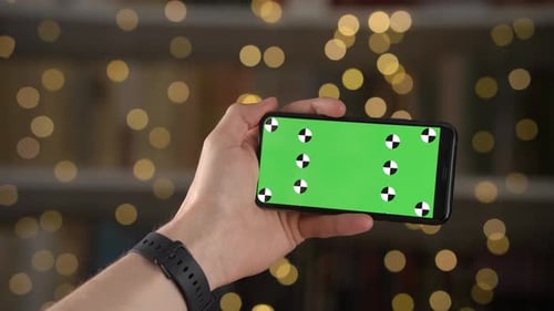 Man Holds Horizontally in Hand Mobile Phone with Chromakey Greenscreen and Swipes Finger on Display