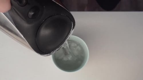 Pouring hot water from a kettle into a cup of tea.