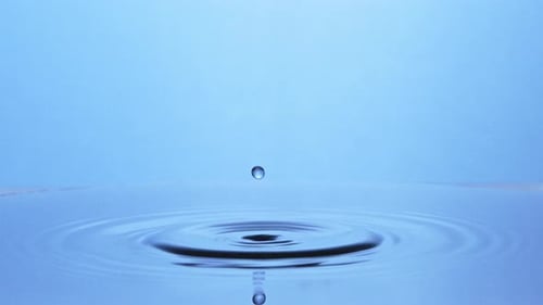 Slow-motion shot, two drops of water falling on light blue surface creating a water pillar.