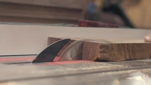 Un morceau de bois est coupé en deux sur une table, scie au ralenti, gros plan.