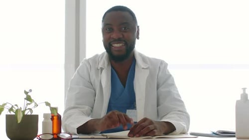 Smiling Doctor Talking to Camera at Desk