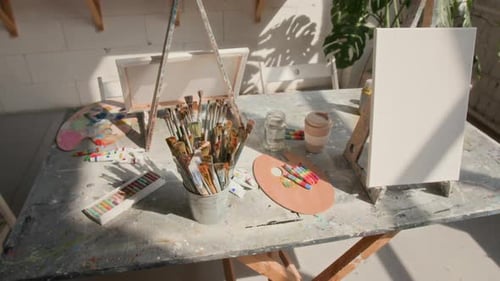 Table with Painting Supplies and Blank Canvas on Stand in Art Studio