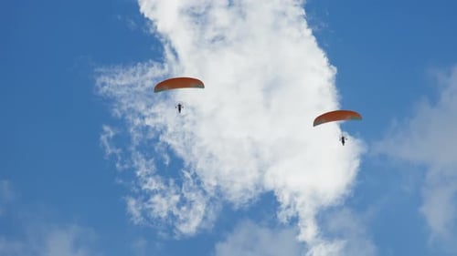 Two Powered Paragliders with Orange Canopies Flying High Clear Blue Sky with Scattered White Clouds