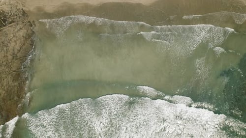 Aerial view of gentle waves along tropical coastline under bright sunlight