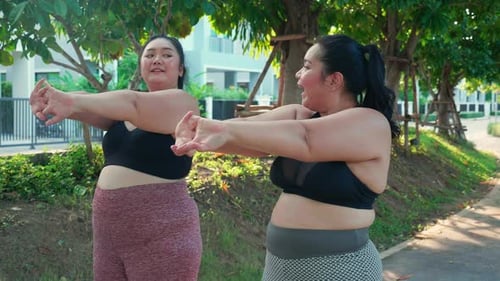 Obese two young asian woman doing stretching arm muscle in the park, woman with overweight warm up,