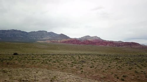 Aerial flying toward the red rocks at Red Rock Canyon with cactus and grasslands in the foreground