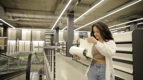 A Young Woman is Looking at Wallpaper and Fabric Samples Holding a Swatch Book