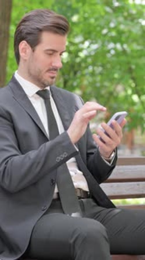 Well-Dressed Man Using Mobile Phone on Park Bench