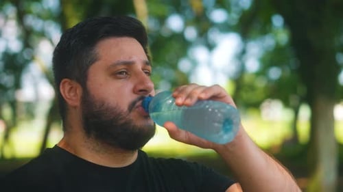 Close up young man drinks water from bottle after jogging in park young healthy person active traini