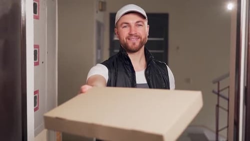 Food delivery man smiles and hands pizza box to customer at apartment door