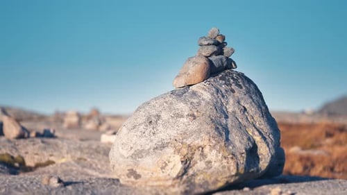 A small stone cairn on the top of a big boulder. More cairns in the background. Slow-motion, pan lef