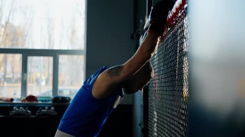 Tired boxer after hard training in the gym wearing sportswear and black boxing gloves