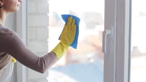 Woman cleaning a window wearing yellow rubber gloves