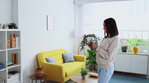 Woman Placing Hanging Plant on Bookshelf in Living Room