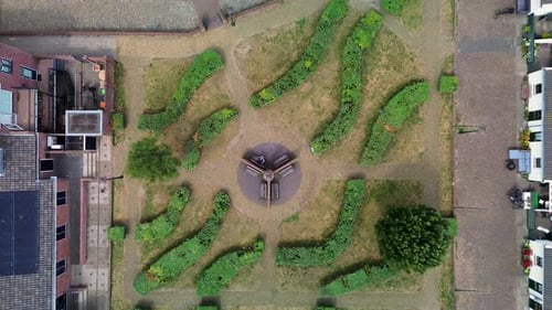 Aerial view of a symmetrical garden courtyard surrounded by houses. Curved green hedges, central