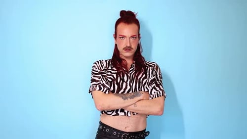 Non-binary person with arms crossed posing on blue background