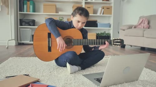 Young Girl Learning Guitar at Home with Laptop
