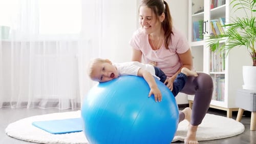 Smiling Woman Supporting Child on Exercise Ball Indoors