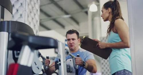 Healthy, active and training strong man working out in the gym with the help of a female personal