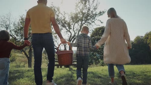Young familly carrying picnic basket and going for a picnic in the countryside field.