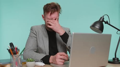Tired Man Rubbing Eyes While Working on Laptop