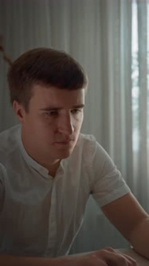 Vertical of Concentrated Man Works on Laptop Sitting at Table in Kitchen