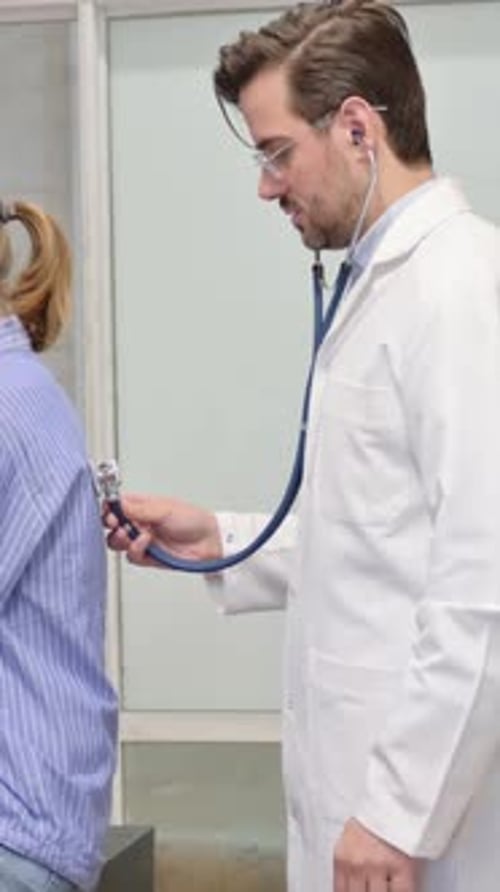 Doctor Listens to Woman's Lungs with Stethoscope in Office