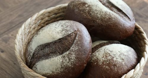 Loaves of bread in wicker basket on wooden table, closeup