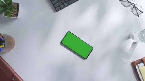 Top down view of a mock up green screen smartphone on a white office desk