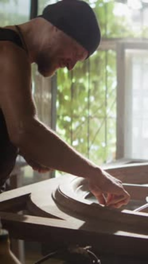 Woodworker in Hat Applies Lacquer Onto Wooden Frame in Workshop