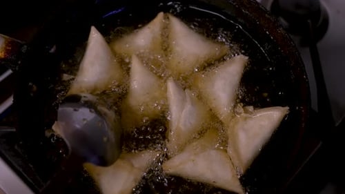 Blick von oben auf Samosas, die in heißem, sprudelndem Öl in einer Bratpfanne gerührt werden. Zeitlupe