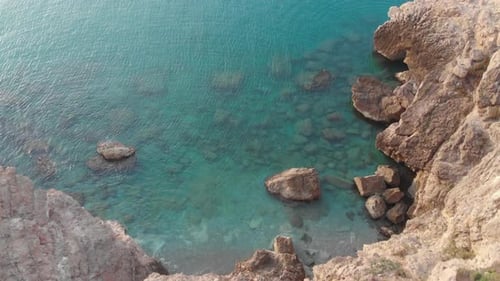 Vista aérea capturada por un Zumbido desde el borde del acantilado, mientras la cámara se eleva sobre un escarpado paisaje de agua azul