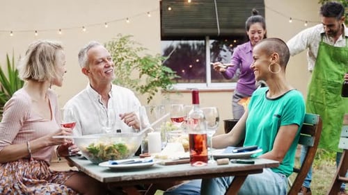 Family Friends Having BBQ Meal Around Table in a Garden in Summer Talking and Laughing