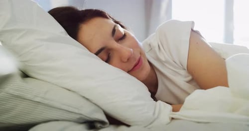 Authentic close up shot of an young brunette woman is sleeping peacefully wrapped in warm duvet bl