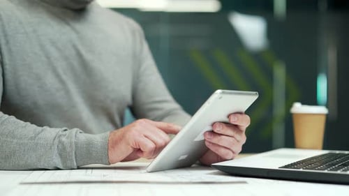 Close up. Man holding a tablet while sitting at a desk at a workplace in a modern office. Employee
