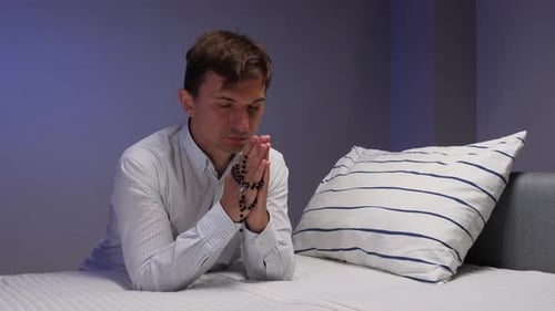Man Praying with Rosary Beads in Bedroom