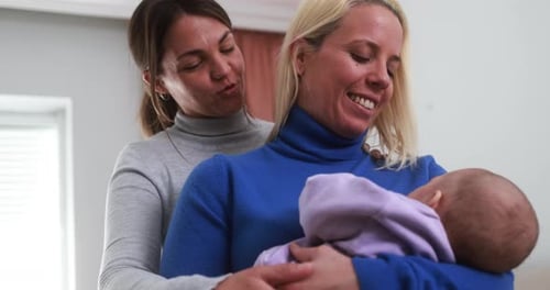 Two women hold infant lovingly in indoor setting