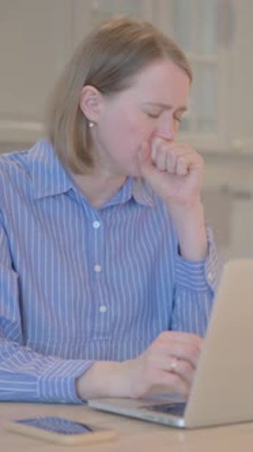 Woman Coughing While Using Laptop at Table Indoors