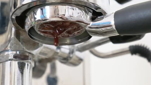Espresso extracting slowly dripping closeup from a bottomless filter in slow motion
