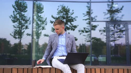 Man Working on Laptop Outdoors Uses Cellphone