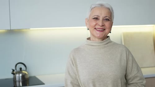 Smiling Senior Woman in Kitchen Wearing Tan Sweater