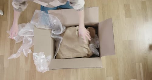 Female person opening package and taking out protective material (air bags). Woman grabs package and