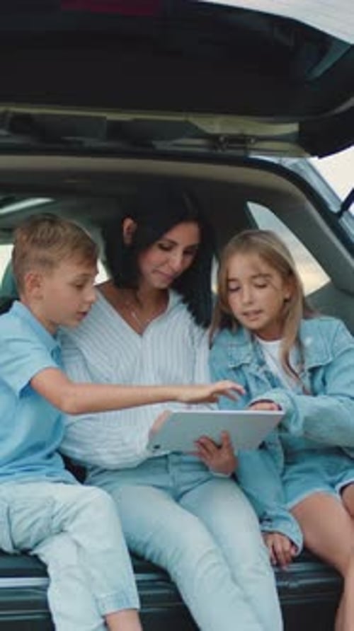 Woman and Children Looking at Tablet in Car Trunk