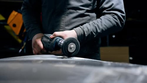 Closeup at a Service Station a Car Mechanic is Trying to Sand Part of the Car