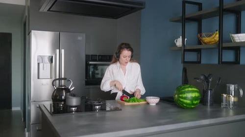 Woman in Headphones Making a Salad of Vegetables and Has Fun Dancing at Modern Kitchen Island Young