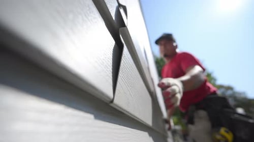 Construction Worker Attaching Siding to House Exterior on Sunny Day