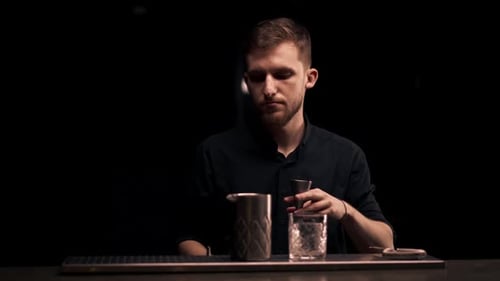 Male Bartender Hands Holding Bottle and Masterfully Pours Beverage Into Steel Jigger on a Black
