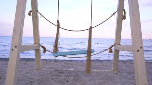 Holzschaukel am Strand, die vor dem Hintergrund des Meeres schwingt. Sonnenuntergang. Eine Möwe fliegt
.
