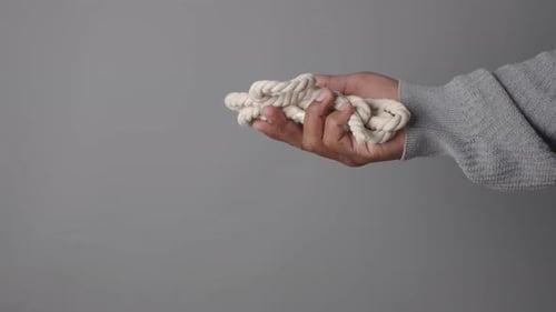 Eine Hand hält fest ein gewundenes Seil vor einem grauen Hintergrund
